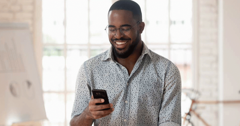 Smiling businessman holding smartphone using apps, standing in an office